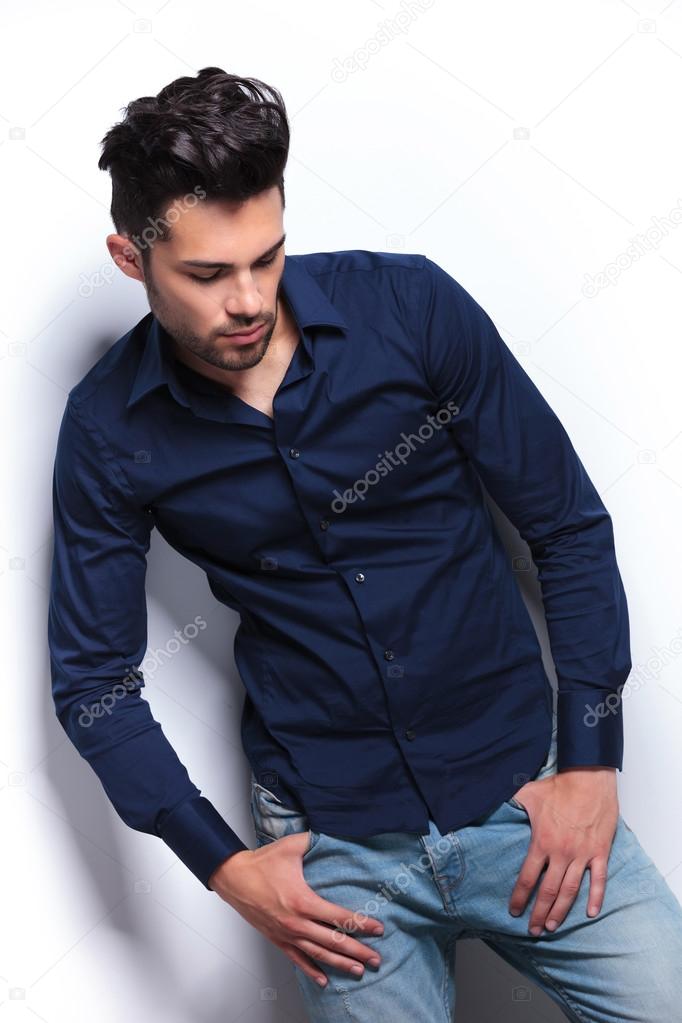young man with thumbs in pockets looks down