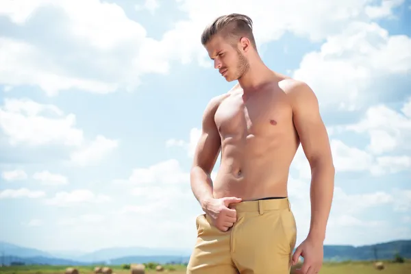 Homme seins nus en plein air avec la main sur pantalon regarde vers le bas — Photo