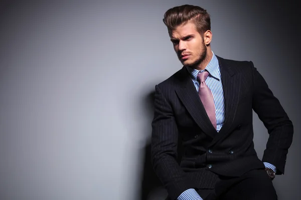 Seated young fashion model in suit looks away — Stock Photo, Image