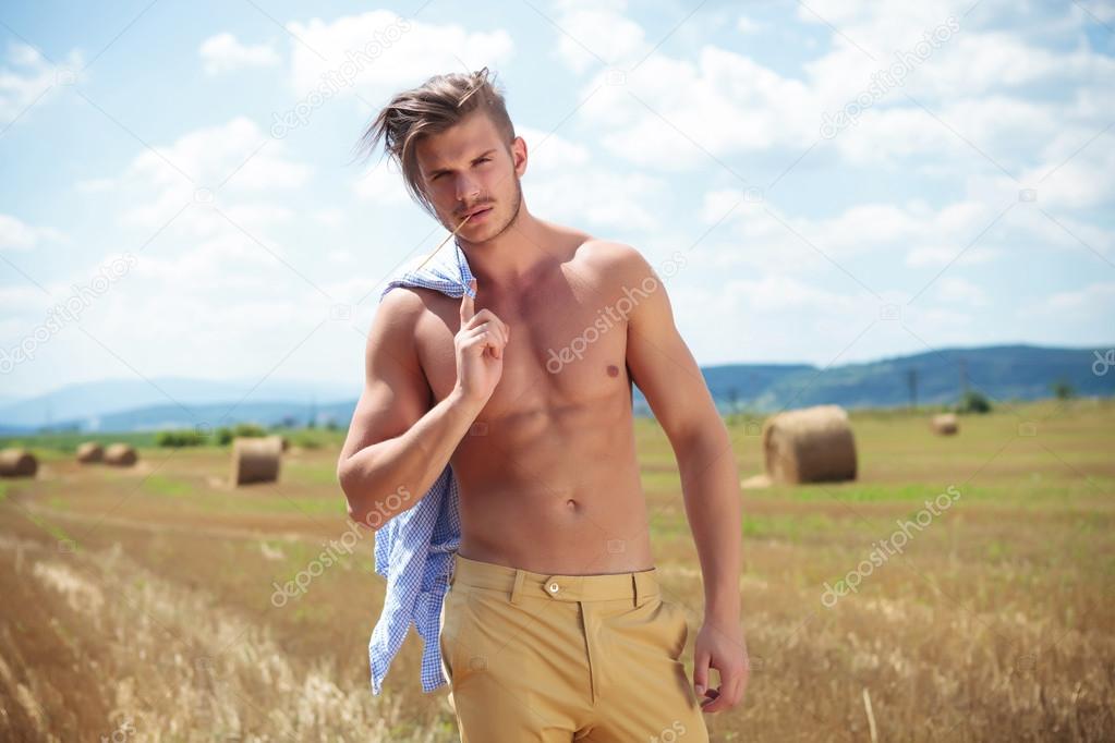 topless man outdoor on a cereal field with a straw in mouth
