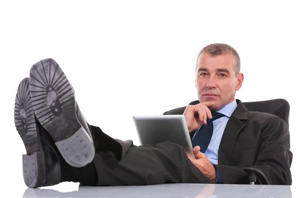 Business man with tablet stands with legs on desk — Stock Photo, Image