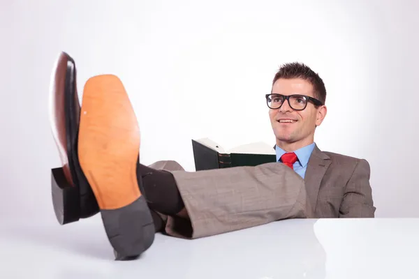 Young business man reads with feet on desk — Stock Photo, Image