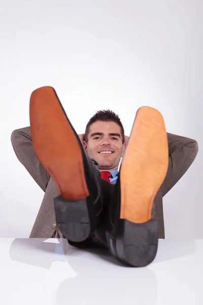 Junger Geschäftsmann lächelt mit den Händen hinter Kopf und Füßen auf dem Kopf — Stockfoto
