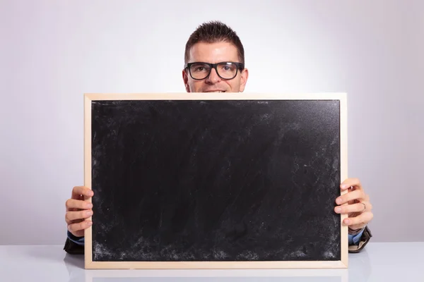 Young business man looks at you from behind blackboard — Stock Photo, Image
