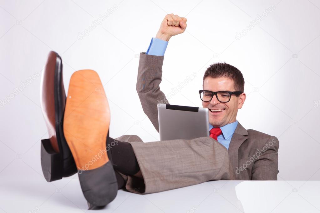 young business man cheers with tablet and feet on desk