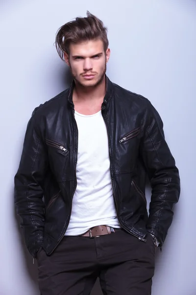 Serious man in leather jacket standing against gray wall — Stock Photo, Image