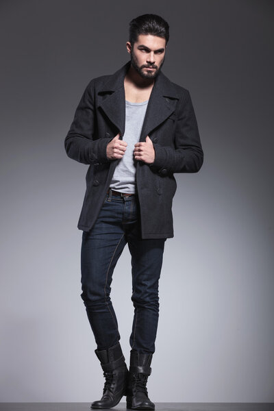 Молодой человек с длинной бородой держит воротник пальто
