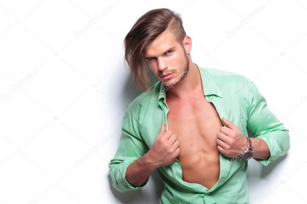 casual man taking off his shirt while looking at you