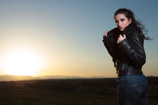 Mujer en chaqueta de cuero y bufanda mirando hacia otro lado en el atardecer — Foto de Stock