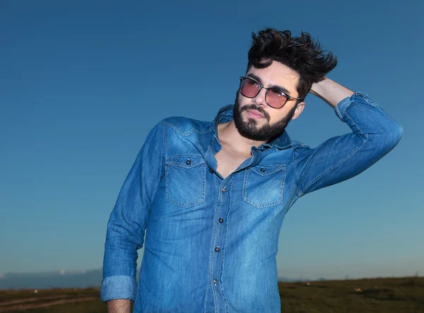 man in blue jeans shirt posing against blue sky