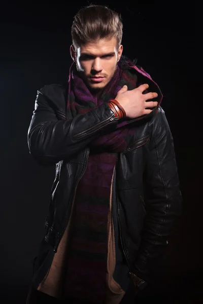 Молодой человек в кожаной куртке регулирует свой шарф — стоковое фото