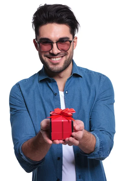 Sonriente joven está ofreciendo una caja de regalo roja — Foto de Stock