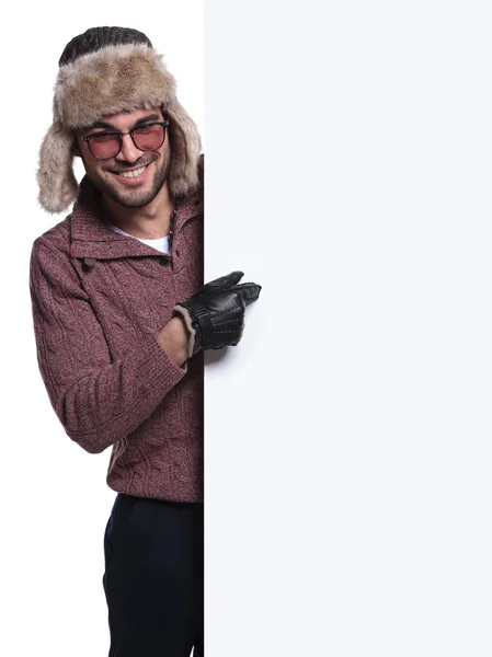 Man in winter clothes and fur hat is pointing to a blank board — Stock Photo, Image