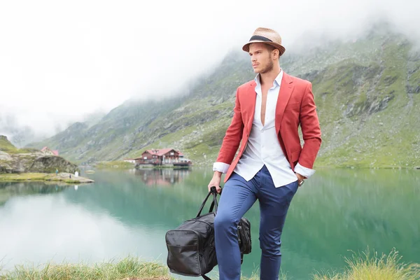 Man met zak wandelen in de buurt van bergmeer met cabine — Stockfoto
