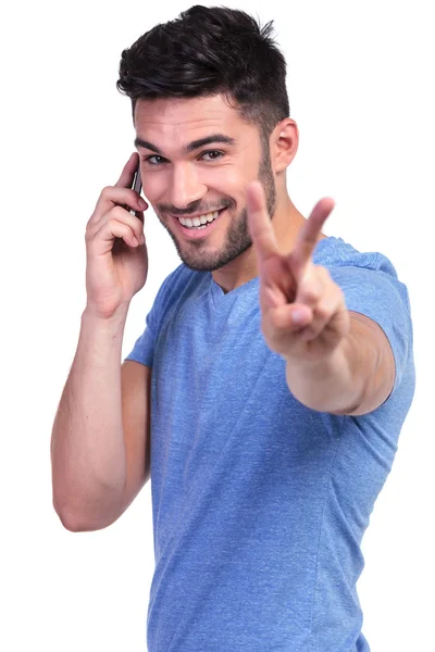 Glücklicher lässiger Mann, der das Siegeszeichen am Telefon macht — Stockfoto