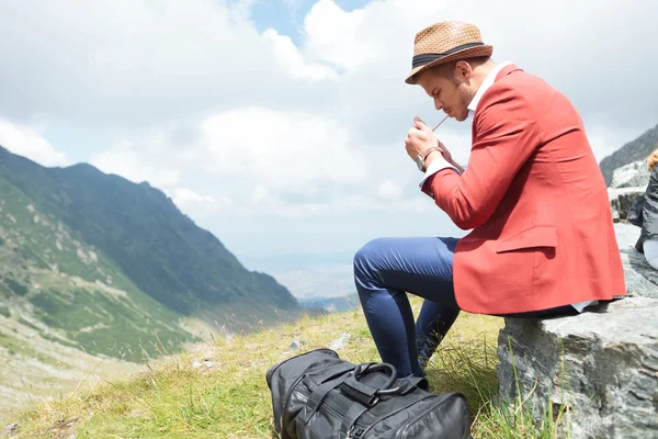 Young man lights cigarette in mountains — Stock Photo, Image