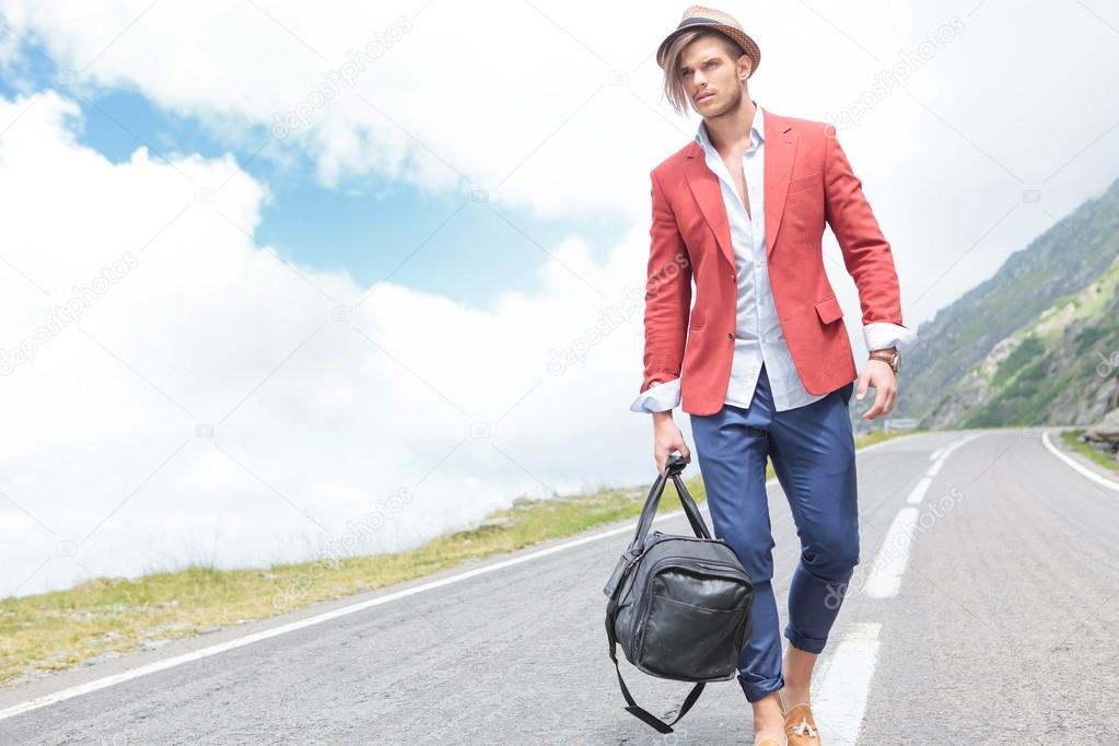 young man strolls outside with bag