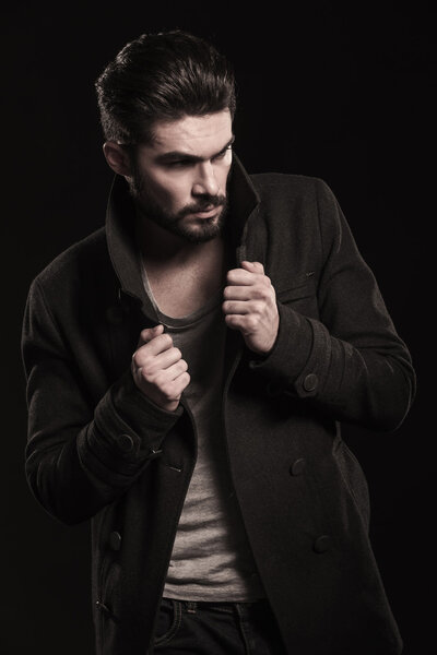fashion young man with beard pulling his coat 's collar
 