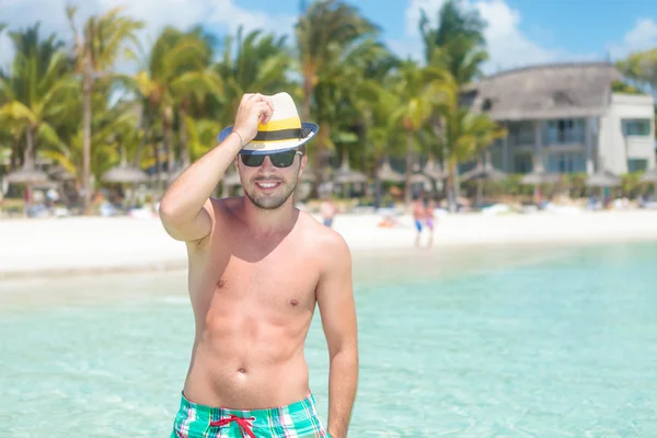 Uomo in costume da bagno tenendo il cappello in spiaggia — Foto Stock
