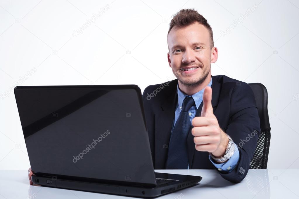 business man shows thumb up behind laptop