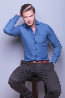 seated fashion man is fixing his hair and smiles