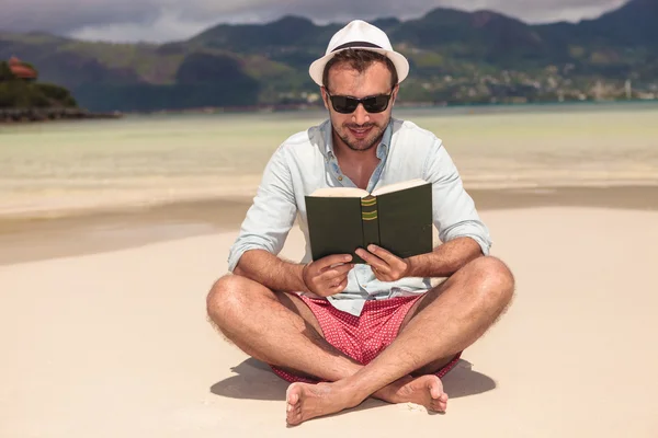 Lächelnder junger Mann liest am Strand ein Buch — Stockfoto