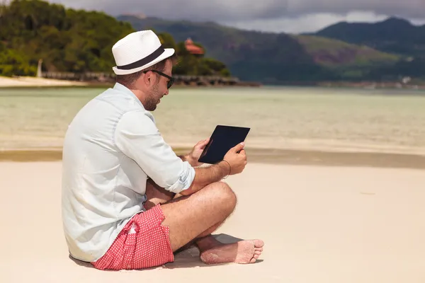 Hombre sentado en la playa y leyendo en la tableta — Foto de Stock