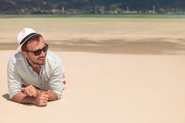 Улыбающийся мужчина лежит на пляже и отводит взгляд — стоковое фото