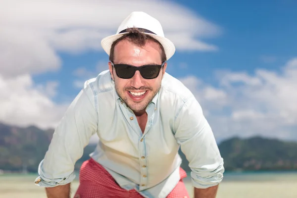 Man med solglasögon och hatt leende på stranden — Stockfoto