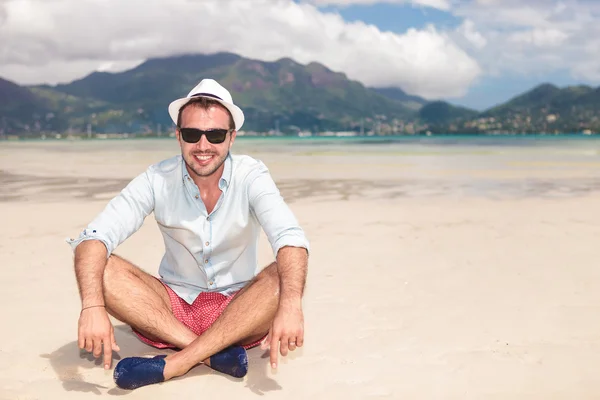 Улыбающийся молодой человек, сидящий на пляже — стоковое фото
