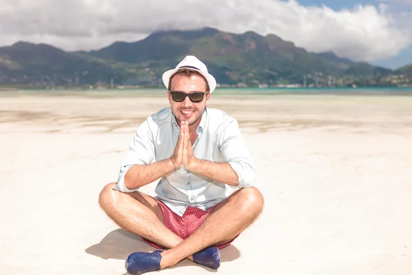 Uomo siede sulla spiaggia e prega — Foto Stock