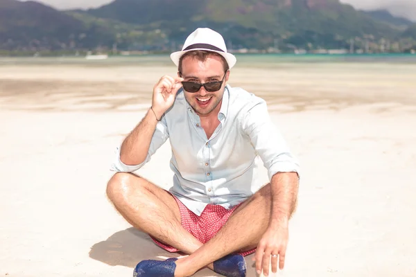 Joven sentado sonriente quitándose las gafas de sol — Foto de Stock