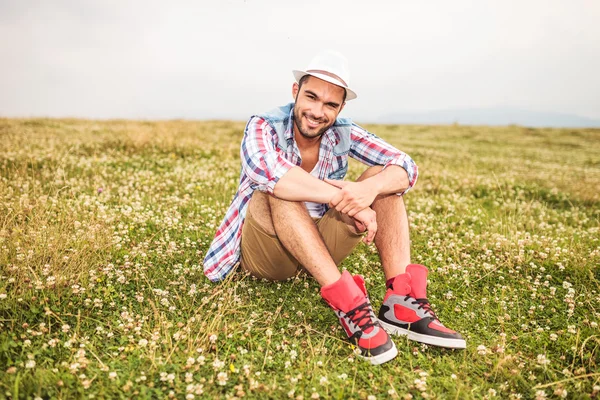 Hombre casual sentado en un campo de hierba y flores — Foto de Stock