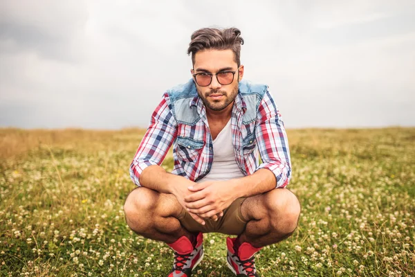 Serio uomo casuale accovacciato in un campo d'erba — Foto Stock
