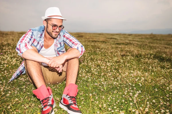 Seated casual man in a field looks down — Stock Photo, Image