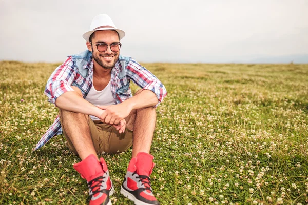 Sonriente joven hombre casual sentado en un campo — Foto de Stock