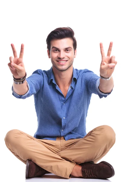 Seated casual man making the victory sign and smiles — Stock Photo, Image