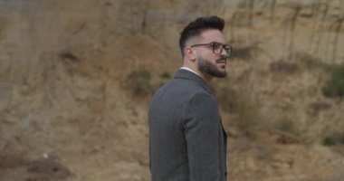 Gri paltolu çekici sakallı adam etrafa bakıyor. Dönüyor, arkasını dönüyor ve doğaya hayranlık duyuyor.