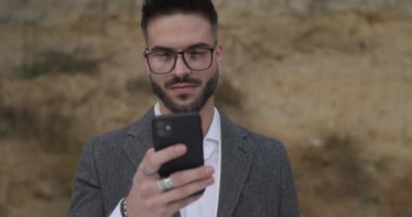 Elinde telefonla havalı tıraşsız bir adam, mesajlar okuyor, gülümsüyor ve parmaklarını kaldırıyor.