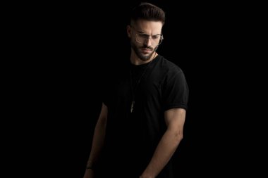 Gözlüklü gizemli adam stüdyoda siyah arka planda poz veriyor.