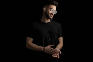 Taraf tutan, avuç içlerine dokunan ve stüdyoda siyah arka planda gülümseyen mutlu sakallı genç adam.