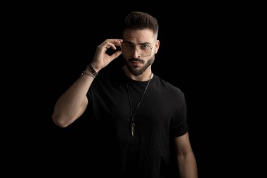 Sakallı, gözlüklü, kendine güvenen ve stüdyoda siyah arka plana karşı duran genç bir manken.