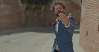 Yakışıklı iş adamı, açık kollu, gülümsemeli, açık havada birini davet ediyor.