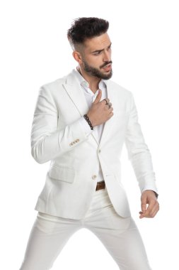 Sert tavırlı seksi manken takım elbisesini onarıp beyaz arka plana bakıyor.