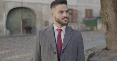 Sakallı zarif bir iş adamı ortaçağ şehir geçmişinin önünde durup gülümsüyor.