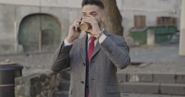 Seksi iş adamı kahvesini içiyor, telefonda konuşuyor, göz kırpıyor ve bardağı kaldırıyor.