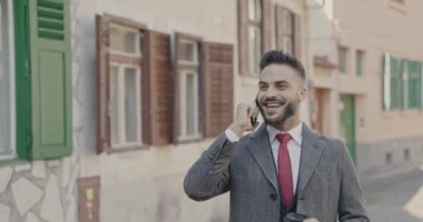 İş adamı cep telefonuyla konuşuyor, yürüyor, gülümsüyor, dışarıda kahvesini içiyor.