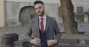 Genç işadamı ceketini kapatıyor ve kameraya gülümsüyor.