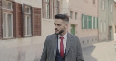 Çekici iş adamı dışarıda yürüyor ve paltosunu kapatıyor.