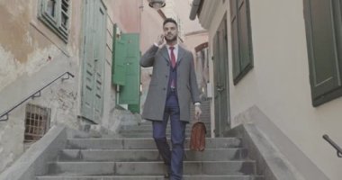 Çekici bir iş adamı merdivenlerden inip elinde bir çantayla telefonda konuşuyor.